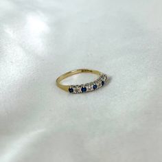 a gold ring with blue and white stones on it sitting on a white cloth background