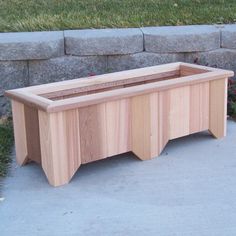 a wooden planter sitting on the side of a sidewalk next to a stone wall