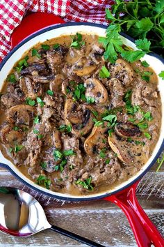 a bowl filled with meat and mushrooms on top of a table next to spoons