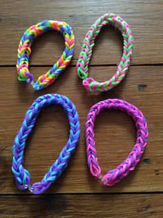 four different colored braided bracelets sitting on top of a wooden table