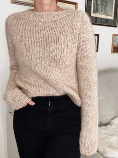 a woman standing in front of a couch wearing black jeans and a beige knit sweater