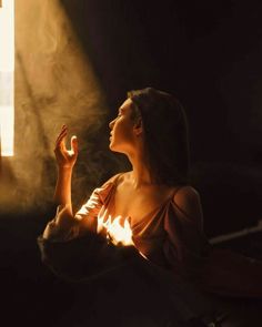 a woman sitting in front of a window holding her hands up to the light coming from behind