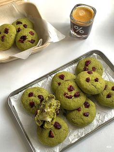 green cookies with cranberries are on a tray next to a cup of coffee