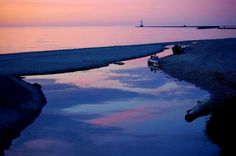 the sky is reflected in the water at sunset near an ocean shore with boats on it