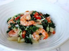 a white bowl filled with shrimp and veggies on top of a marble table