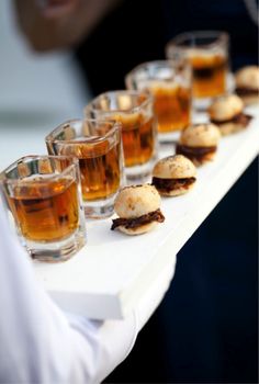 there are many small sandwiches and drinks on the trays with people in the background