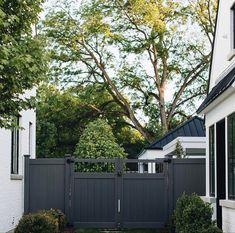 a black fence in front of a white house with trees and bushes on the side