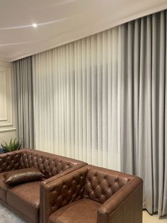 a brown leather couch sitting in front of a window with curtains on the windowsill