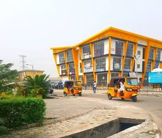 two yellow tuk tuks parked in front of an orange and white building on the street