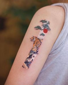 a woman's arm with a tiger and pine tree tattoo on the left shoulder