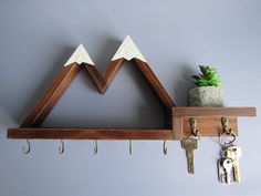 a wooden shelf holding keys and a potted plant on it with two mountain shaped decorations