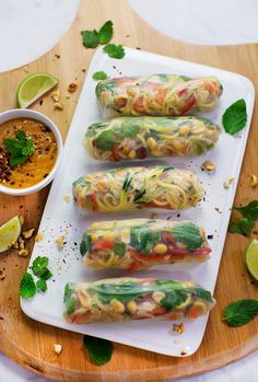 four vegetable rolls on a plate with dipping sauce and garnished with fresh herbs