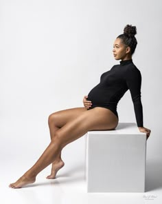 a woman is sitting on top of a white block and posing for the camera with her legs crossed