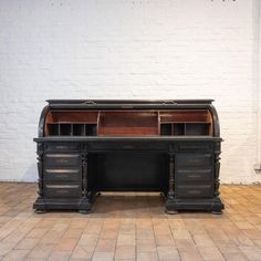 an old black desk with two drawers and a book shelf on the top, in front of a white brick wall