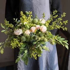 a woman in an apron holding a bouquet of flowers and greenery on her hands