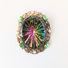 "This vintage, mid century brooch dates to the 1960s.  It features a large, oval rhinestone with watermelon colors in hot pink, blue, yellow and green. The glass stone is set in an ornate gold tone setting embellished with light green marquis shaped rhinestones and faux pearls. I don't see a maker's mark on this dramatic piece.  Measurements: It measures 2-3/16\" in tall and 1-3/4\" wide. Condition: There is a hole at the top of the watermelon stone, but that appears to have been present when th Watermelon Stone, Pink Blue Yellow, Maker's Mark, Yellow And Green, Vintage 1960s, In Hot, Makers Mark, Blue Yellow, Faux Pearl