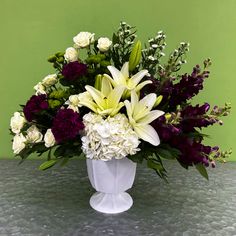 a vase filled with white and purple flowers on top of a table next to a green wall