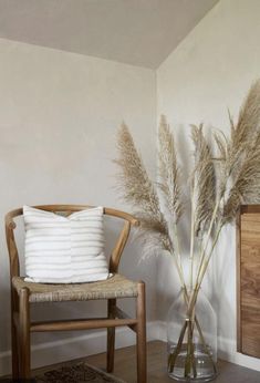 a wooden chair sitting next to a vase filled with dry grass on top of a hard wood floor