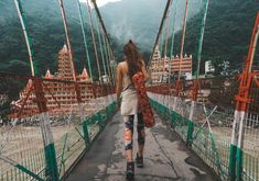 a woman walking across a suspension bridge with mountains in the background