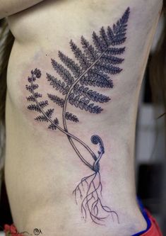 a woman's lower back with a fern tattoo on her stomach and roots growing out of it