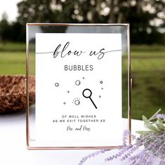 a close up of a sign on a table with flowers in the foreground and a basket behind it