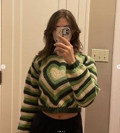 a woman taking a selfie while wearing a green and white knitted heart sweater