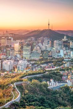 the city skyline is shown at sunset with mountains in the backgrouund and trees on both sides