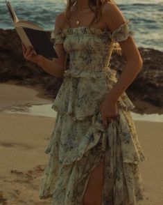 a woman in a dress holding a book on the beach