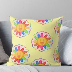 a yellow pillow with colorful flowers and smiley faces on the front, sitting on a couch