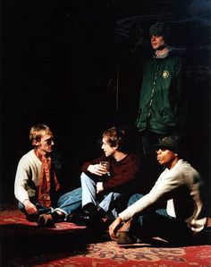 four young men sitting on the floor in front of a black background