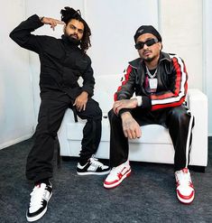 two young men sitting on a white couch wearing black and red striped clothing, one with dreadlocks