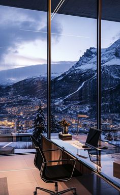 an office desk with a view of the mountains and city lights at night, in front of large glass windows