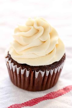 a chocolate cupcake with white frosting on a red and white table cloth next to a fork