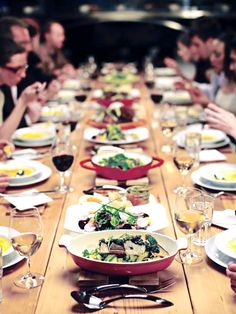 people sitting at a long table with plates and glasses on it, all eating food