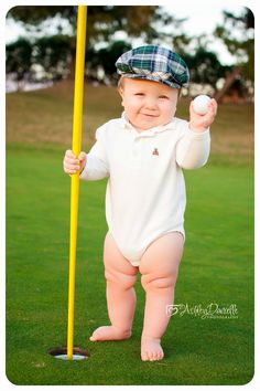 a baby standing on the grass holding a baseball bat