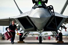 a fighter jet sitting on top of an airport tarmac next to a man with luggage