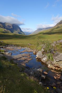 there is a small stream in the middle of this field with mountains in the background