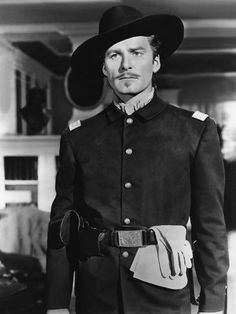 a man wearing a uniform and hat standing in front of a building with his hand on his hip