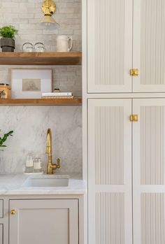 a kitchen with white cabinets and marble counter tops, gold faucets and brass pulls