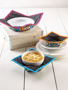 two bowls with noodles in them on top of a wooden box next to plates and napkins