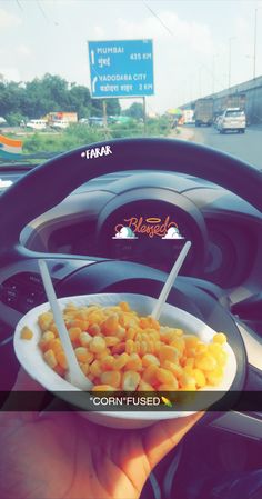 a person holding a plate of food in their hand on the steering wheel of a car