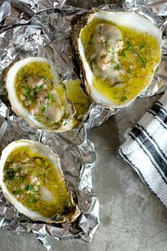 three open oysters sitting on top of tin foil covered in green sauce and garnished with parsley