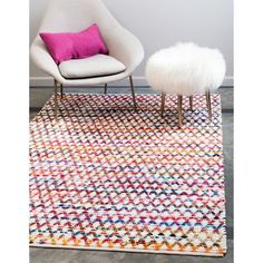 a white chair sitting on top of a wooden floor next to a rug with a pink pillow