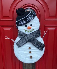 a snowman door hanger on the side of a red door with a black hat and scarf