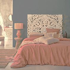 a bed with pink sheets and pillows on top of it next to a white headboard