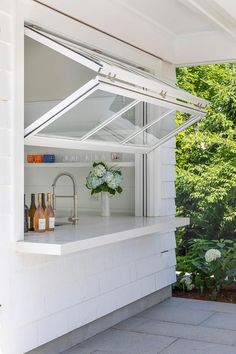 an outdoor kitchen with white cabinets and counter tops, under a glass roof over the sink