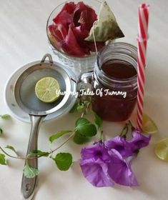 two jars filled with liquid next to flowers and a spoon on a white table top