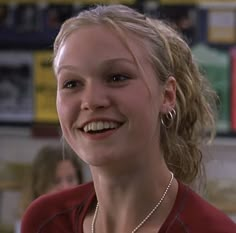 a woman with blonde hair wearing a red shirt and smiling at someone in the background