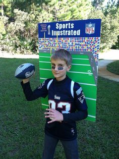 a young boy with his face painted like a football player holding a ball and posing in front of a sports sign