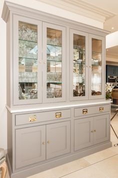 a gray china cabinet with glass doors and gold handles in the middle of a room